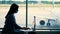 Dark silhouette of businesswoman in mask, working on laptop against panoramic window, at airport, while waiting for
