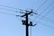 Dark silhouette of concrete electrical utility pole with multiple electrical wires connected over glass insulators on blue sky