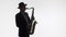 Dark silhouette of a elegant musician playing gold saxophone on a white background of the studio. Artist in hat and suit