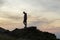 Dark silhouette of a hiker on a mountain at sunset standing on summit like a winner