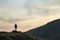 Dark silhouette of a hiker on a mountain at sunset standing on summit like a winner