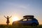 Dark silhouette of lonely woman relaxing near her car on grassy meadow enjoying view of colorful sunrise. Young female driver