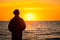 Dark silhouette of a man standing by the sea at golden sunset. Lonely teenager looking a setting sun