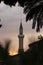 Dark silhouette of a mosque with a tall minaret at sunset.