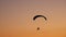 Dark silhouette of Moto Paraglider flies, soars in the air, against the background of a bright orange sunset