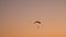 Dark silhouette of Moto Paraglider flies, soars in the air, against the background of a bright orange sunset