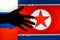 Dark silhouette of outstretched hand on background of flags of Russian Federation and North Korea