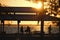 Dark silhouette of people resting under alcove roof on sea shore in public park at sunset