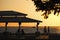 Dark silhouette of people resting under alcove roof on sea shore in public park at sunset