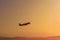 Dark silhouette of a plane is gaining altitude over a city. Against a background of orange sky with smog and polluted air.