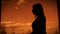 Dark silhouette of a woman standing in profile on twilight backcloth near the window. Outline of female body against