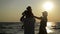 Dark Silhouettes of Mother in Summer Hat and Father with Little Daughter near the Sea During Sunset. Strong Man Swirls