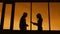 Dark silhouettes of slim woman and man standing in profile on twilight near the window. Outline of female businesswoman