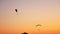 Dark silhouettes of two Moto Paragliders fly, soar in the air, against the background of a bright orange sunset