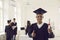 Dark-skinned african-american graduate standing with diploma and raises thumb up looking at camera.