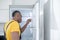 Dark-skinned service man in yellow tshirt standing near the fridge