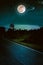 Dark sky with full moon and roadway through suburban zone.