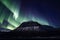 Dark snow covered mountain with aurora borealis above. Northern lights.