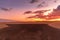 Dark sunset overlooking the ocean and orange sunset and the sand dunes and leaves of the dappled trees moving in strong wind