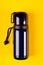 Dark thermos composition on yellow background. Flat lay