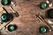 Dark turquoise glazed clay teapot and small cups on dark wooden background decorated with white flowers. Flat lay style