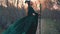 Dark witch stands on forest path in long flying emerald dress free flying sleeves with a golden belt. lady with magic