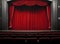 Darkened empty movie theatre and stage with the red curtains drawn viewed over rows of vacant seats from the rear