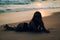 The darkened silhouette close-up shot of a girl lying on her stomach on white sand in a swimsuit near the water at