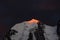 Darkness mountain landscape with great snowy mountain lit by dawn sun among dark clouds. Awesome alpine scenery with high mountain