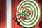 Darts target with many arrows hanging red wooden wall