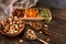 Dates, dried apricots and kiwis in a Compartmental dish and assortment of nuts in wooden bowl on a dark wooden table