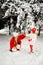 Daughter blows snow from a spruce branch onto her mother. mom and daughter blonde on a background of snow and large Christmas