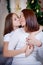 Daughter kissing and hugging mother under Christmas