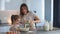 Daughter and mother cooking together. Woman is hands pour the milk to dough for kneading. Mom is assistant a little