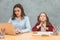 Daughter and mother on a gray background. During this, the girl puts the yellow pencils in her mouth. Mom carefully