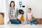 daughter in pink t-shirt and mother in grey shirt sitting on floor near scattered  clothes and washer