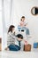 daughter in t-shirt sitting on washer with digital tablet wile mother in grey shirt taking clothes from basket