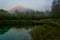 Dawn illuminated mountains reflecting in forest lake.