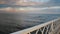Dawn light bathes ocean, waves gently roll in. View from weathered white railing of pier, serene seascape at sunrise