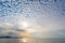 Dawn on the sea with a sky of small white clouds.