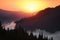 Dawn view in the mountains. Fog among the mountains, a green coniferous forest on the slopes and the sun rising from