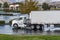 Day cab white big rig semi truck delivering food cargo in refrigerator semi trailer to local customer standing on the parking lot