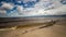 Daytime timelapse on the sandy beach. A log in the foreground. Waves roll on the other.