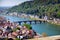 Daytime view of Heidelberg from a height. Bridge, river Necka, old town, trees with green leaves, mountain, maroontiled roofs.