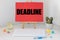 `Deadline` inscription on a red card on an office table, alarm clock showing the time at five to twelve, Last minute concept at th