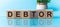 DEBTOR - word from wooden blocks with letters, to divide or use something with others share concept, blue background