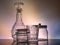 A decanter, a glass and glass jars standing on a stand with reflection with unusual lighting