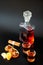 A decanter and two glasses of cognac next to chocolates, cinnamon and mandarin slices on a black background