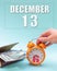 December 13th. Hand holding an orange alarm clock, a wallet with cash and a calendar date. Day 13 of month.