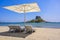 Deck chair and umbrella on beautiful Agios Stefanos Beach in front of paradise Island Kastri- historical ruins and paradise